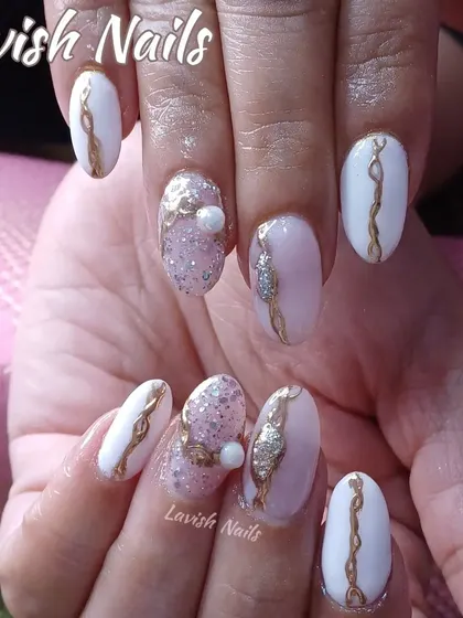 An ornate design featuring white and pink nails with gold swirls, glitter, and 3D pearl and rhinestone accents.