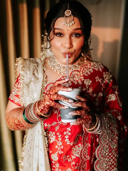 A candid and fun moment of the bride sipping a drink, fully decked out in her bridal attire.