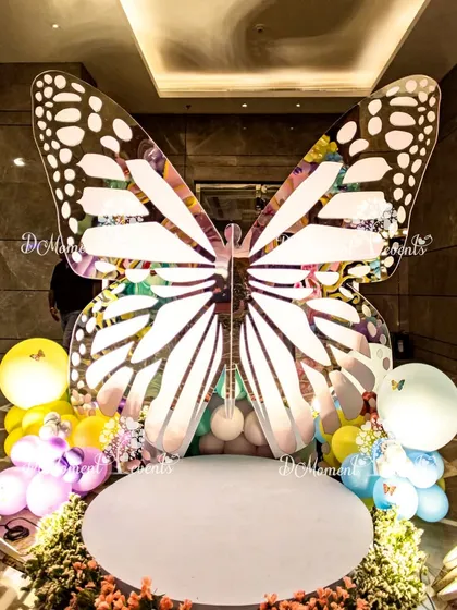 A stunning, oversized butterfly prop serves as a unique photo booth. The intricate wing design and surrounding floral and balloon decor create a perfect spot for memorable pictures.