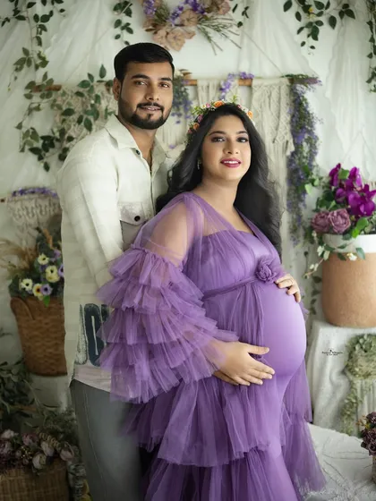 A classic couple's portrait in our bohemian studio. They stand together, hands on the baby bump, looking at the camera with happy and hopeful smiles.