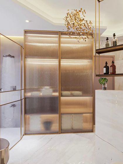 A master bathroom design that feels open and luxurious. The space features fluted glass partitions, a freestanding tub, and a beautiful gold chandelier.