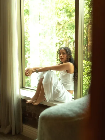 A quiet, contemplative moment sitting in a windowsill. The lush greenery outside provides a beautiful, natural backdrop.