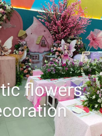 A close-up of the fairy-themed birthday party decor. The setup includes a miniature fairy house, cherry blossom trees, and adorable character cutouts amidst the floral arrangements.
