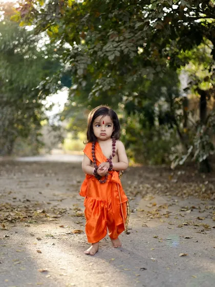 A full-length shot of a little girl dressed as Ram, standing barefoot on a path in the woods. The natural setting adds a beautiful, authentic feel to this Ram Navami themed shoot.