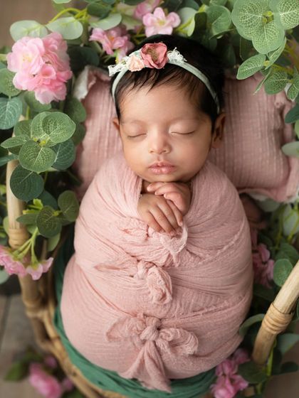 A newborn girl wrapped in a pink swaddle, nestled in a basket of flowers. This image is a beautiful celebration of new life, painted in soft, gentle colors.