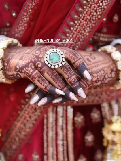 A close up shot focusing on the rich color of the henna stain. The dark color makes the intricate details of the finger designs and the large ring stand out beautifully.