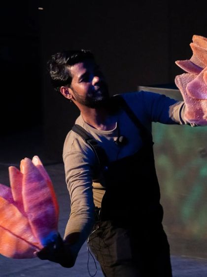A puppeteer performs a dance with flower-like hand puppets in 'Aisha's Journey'. The show combines different forms of puppetry and movement to create a rich visual narrative.