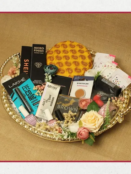 A beautiful makeup hamper presented on a golden, heart-shaped tray. This collection includes products from Lakmé, Recode, and other popular brands, surrounded by delicate floral decorations.