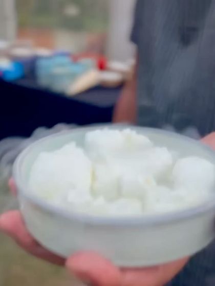 A hand holds out a small bowl of a white, smoky concoction from our chaat station. This image captures the personal interaction and the element of culinary magic that defines our service.