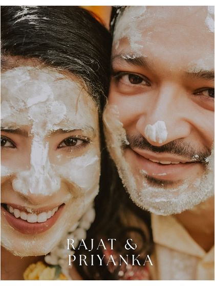 A close-up selfie-style portrait of the couple, their faces covered in haldi paste, smiling together.