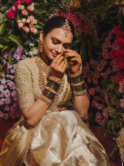 A bride surrounded by flowers, her hands adorned with henna. Her golden saree and blouse are a perfect match for the festive and celebratory atmosphere.