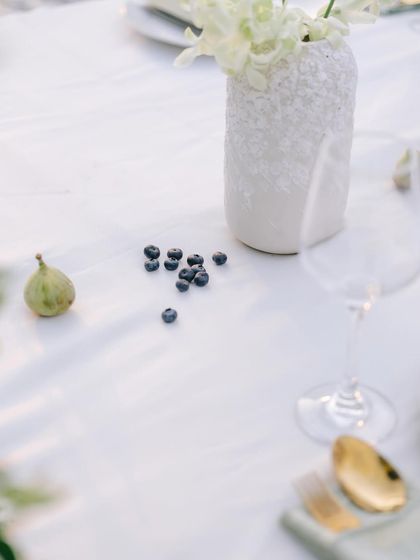 A minimalist detail from the tablescape, with a few scattered blueberries and a fig next to a textured white vase.