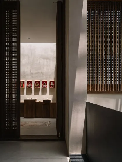 A view through a slatted wooden door into the serene puja room. The design emphasizes natural materials and a sense of tranquility, creating a spiritual corner within the home.