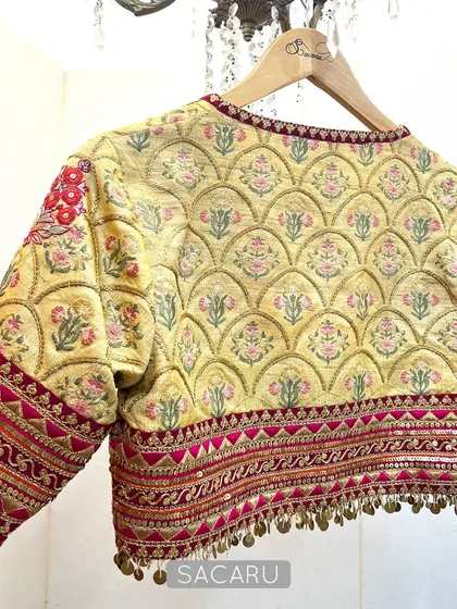 We love to play with color and texture. This blouse is an artistic expression, featuring quilted fabrics, vibrant prints, and detailed hand embroidery with brass sequins and mirror work, designed to pair with a designer saree.