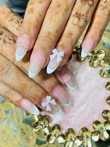 Elegant stiletto French tips with an ombre base, accented with 3D white bows and a delicate line of pearls along the cuticle.