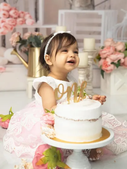 A radiant smile from the birthday princess. Dressed in a beautiful lace gown, she is surrounded by a soft, romantic floral setup, perfect for her first birthday photos.