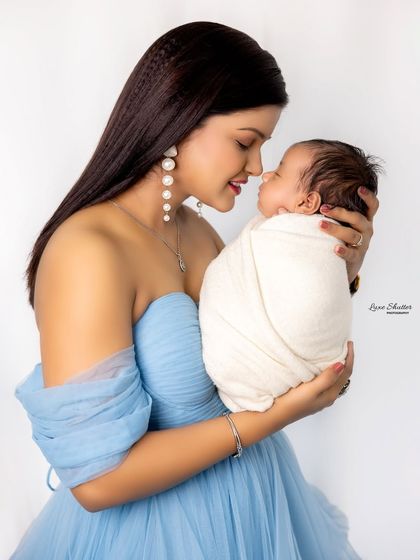 A beautiful close-up of a mother and her newborn. The mother's elegant blue dress and pearl earrings add a touch of sophistication to this tender portrait.