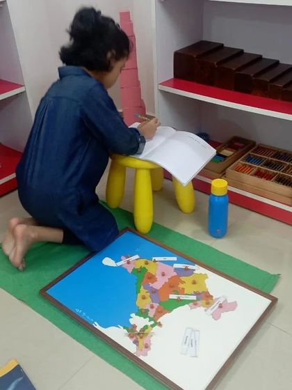 Language work is integrated with other areas. Here, a child uses the India map puzzle and then writes the names of the states, combining geography with literacy skills.