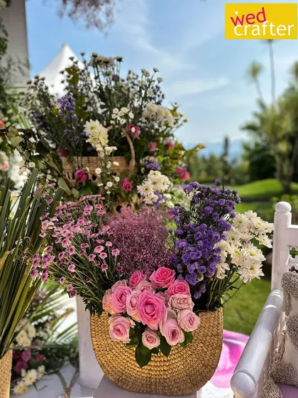 A beautiful arrangement of pastel pink, purple, and white flowers in a woven gold basket, adding a touch of rustic elegance.