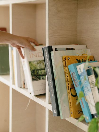 A hand reaching for a book on modern Indian cooking from our curated shelves. Our collection includes everything from cookbooks that inspire me to fiction and non-fiction that make you think.