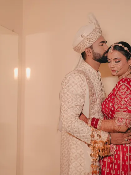 A quiet, intimate moment captured indoors. The groom's tender forehead kiss shows his love and affection for his bride.