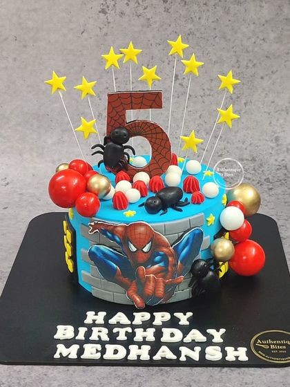 A heroic Spiderman cake for a 5th birthday. This design features Spiderman in action, surrounded by stars, spiders, and colorful spheres.