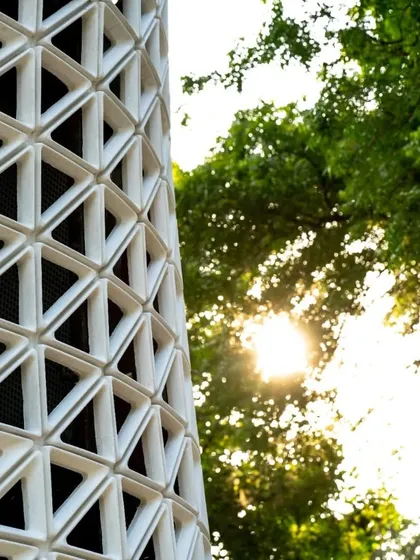 The sun filters through the trees, highlighting the texture of the VERTO tower. The material used is durable and weather-resistant, ensuring the product's longevity and performance in an outdoor public setting.