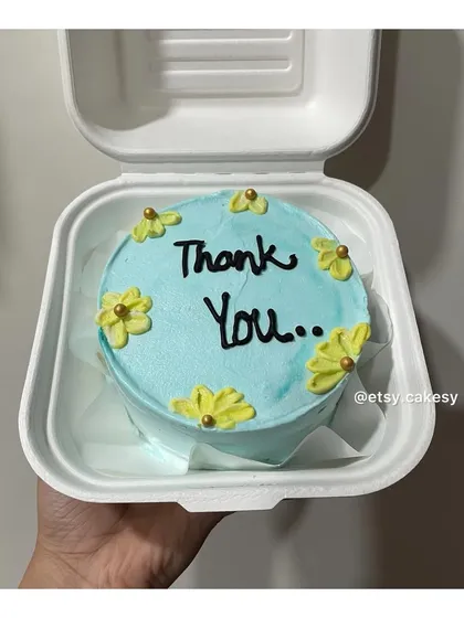 A simple blue bento cake with a 'Thank You' message and small yellow flowers. A sweet way to show gratitude.