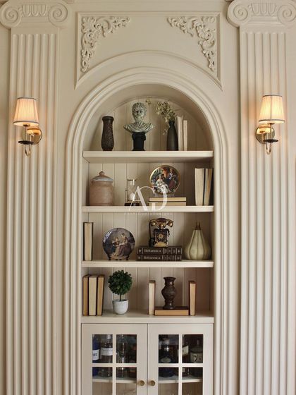 A symmetrical view of the central bookshelf, flanked by fluted pilasters and ornate corner details. The warm light from the wall sconces highlights the craftsmanship of the millwork.
