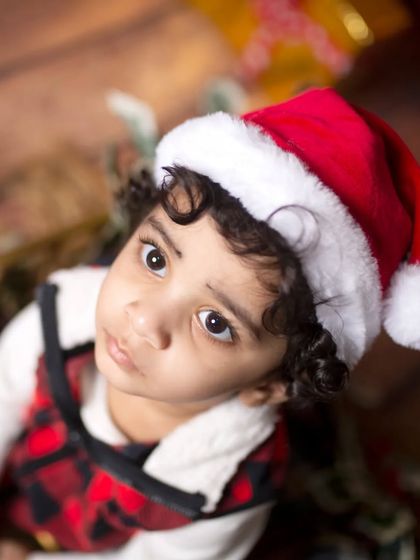 A beautiful, soft-lit close-up of a toddler in a Santa hat, capturing the wonder of the holiday season.