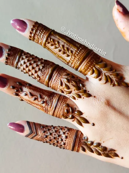 A close-up of detailed finger henna, showcasing different filler patterns and leafy vines.