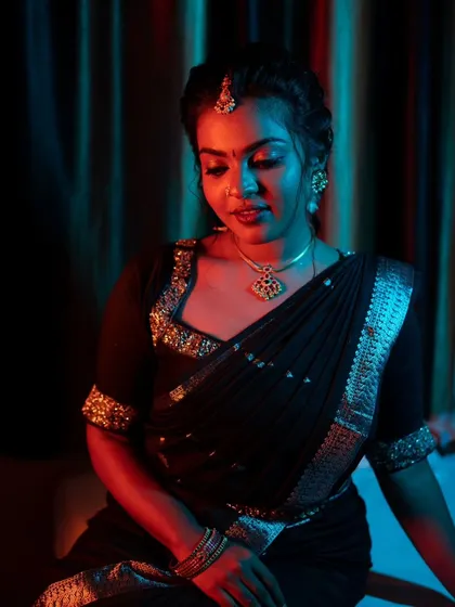 A dramatic shot of a model in a black saree, with red and blue lighting creating a moody and artistic effect.