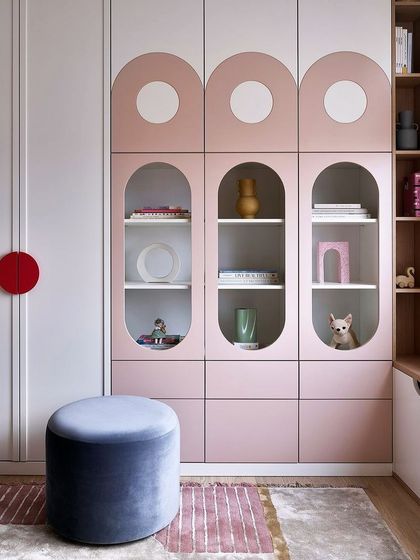 This playful wardrobe design is perfect for a kids' room. It features curved shutters with circular glass cutouts and a soft pink and white color palette, combining fun aesthetics with practical storage.