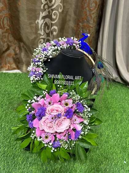 A beautiful baby shower prop set, including a floral purse and a matching hairpiece with a peacock motif, all made from real flowers.