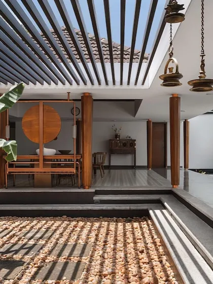 Light and shadow play across a dry pebble courtyard under a slatted pergola, a modern interpretation of a traditional architectural element.