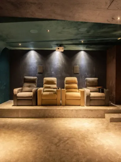 This home theater uses rich, textured wall finishes and tiered seating to create an intimate and luxurious viewing room. The dark color palette and focused spotlights enhance the cinematic feel.