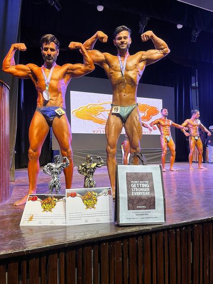 My two men's physique champions posing with their medals and trophies. Their success shows the effectiveness of our customized training and nutrition plans.