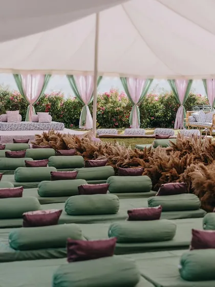A wide view of the floor seating arrangement for a serene Anand Karaj. The rows of green mattresses and cushions are set under a large tent, with pampas grass lining the central aisle.