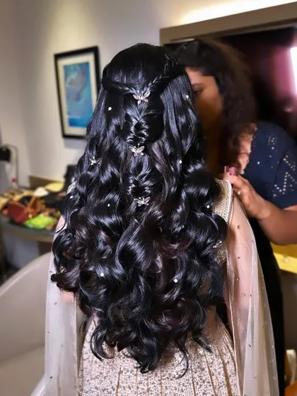 A reception hairstyle featuring a waterfall braid and soft curls, adorned with butterfly clips.