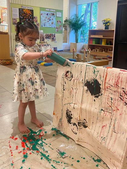 Using a large syringe filled with paint, this child experiments with gravity and motion. She observes how the paint drips and flows, learning about physics and cause and effect in a dynamic and artistic way.