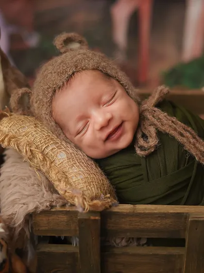 A smiling newborn dreams of a jungle adventure. This safari-themed shoot features a cute animal hat and a rustic wooden cart.