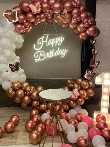 A beautiful first birthday setup with a rose gold and white balloon ring, butterfly accents, and a light-up number '1'.