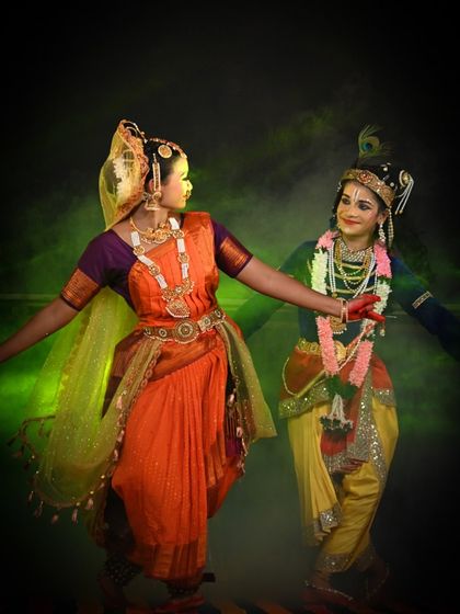 A playful and enchanting moment between Radha and Krishna, set against a magical green-lit background. The chemistry between the dancers brings the divine love story to life.