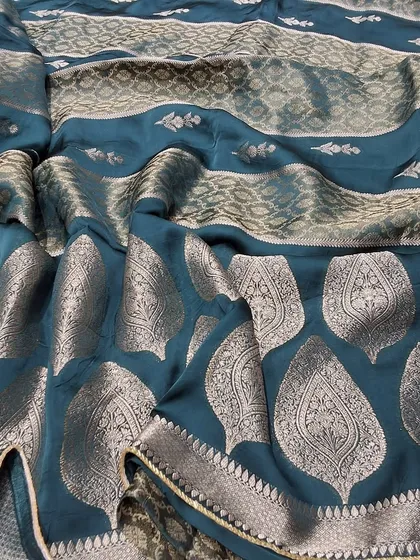 The beautiful drape of a teal green soft silk saree with intricate silver zari work. This fabric is known for its softness and sheen, making it both comfortable and glamorous.
