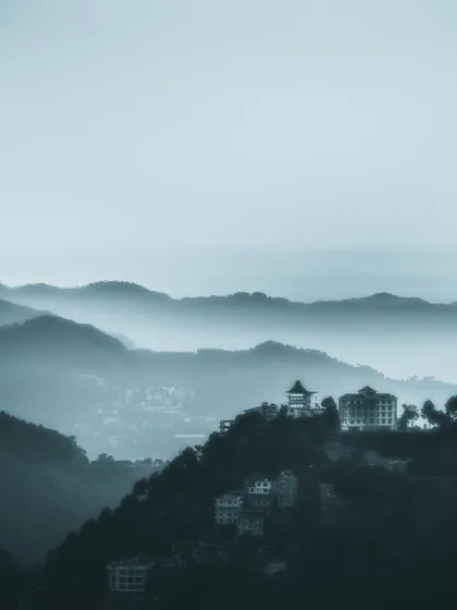 a distant building perched on a misty mountain range. this photo plays with atmospheric perspective, creating a sense of scale and distance.