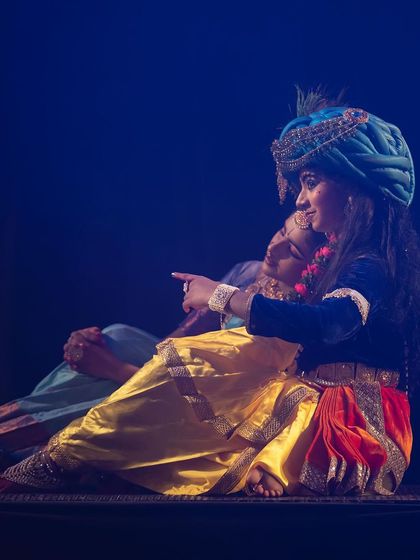 A quiet, intimate moment from "KRISHNA", where the characters share a story. The detailed costumes and expressive gestures convey the narrative without a single word.