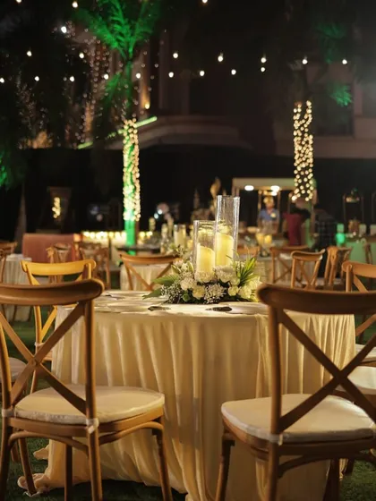 An intimate table setting at an outdoor engagement party. The wooden cross-back chairs and simple floral centerpiece with candles create a rustic yet elegant feel, perfect for a celebration under the stars.