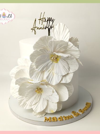Pure elegance in every petal. This minimalist white anniversary cake is adorned with large, beautifully crafted white sugar flowers, creating a statement of timeless love.