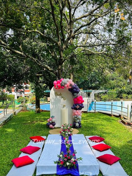 An outdoor bachelorette party by the pool. We set up a picnic-style dining area and a modern arched backdrop with a balloon garland in shades of pink, grey, and purple.