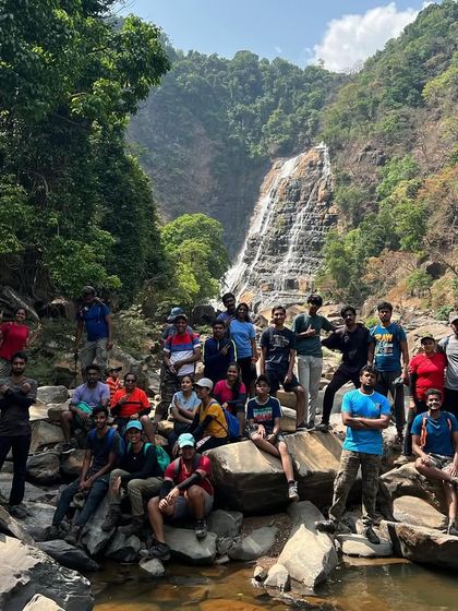 A group photo from a summer trek, with a beautiful waterfall in the background, showing that adventure is available year-round.